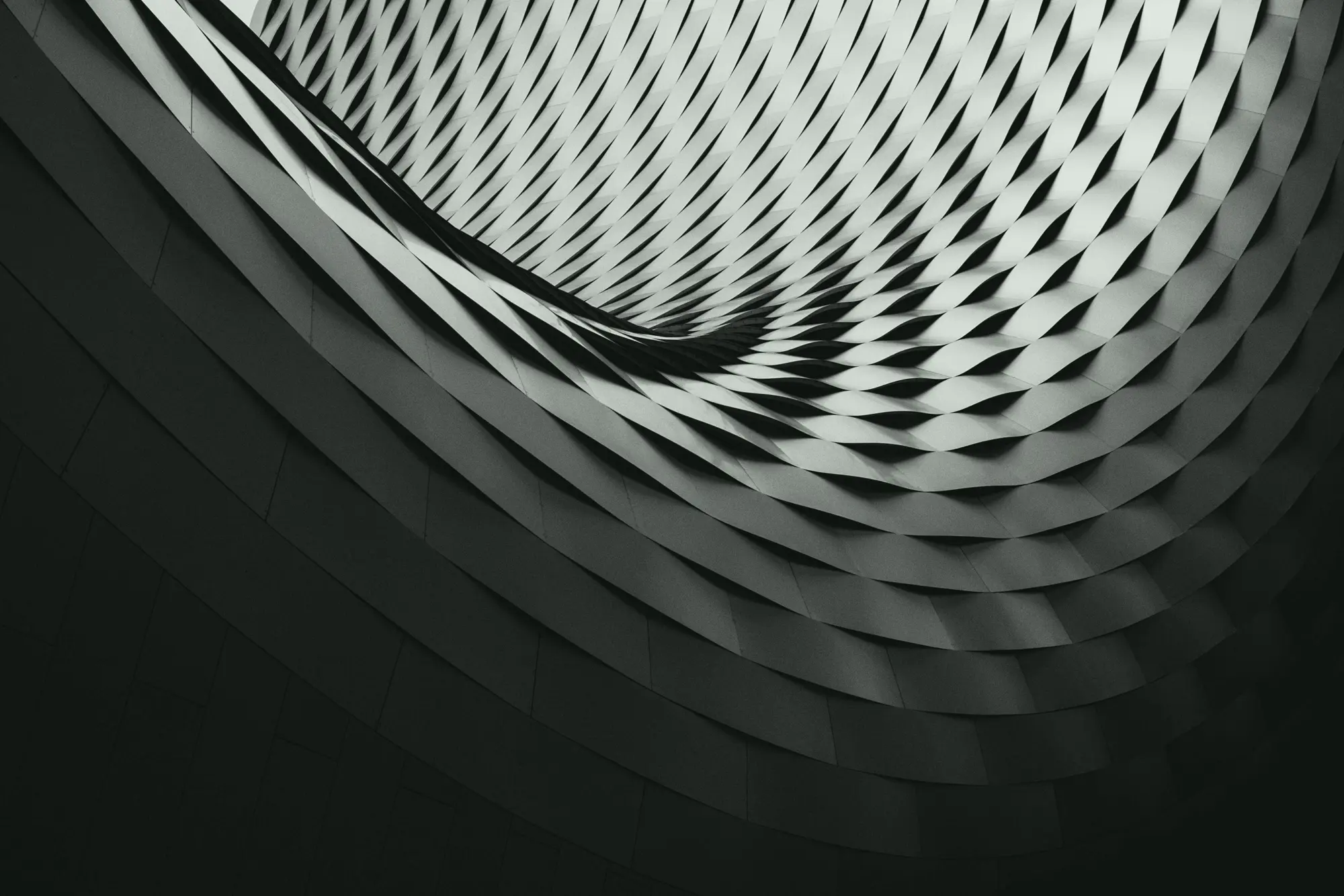 A woven metal facade curving overhead in repeating bands