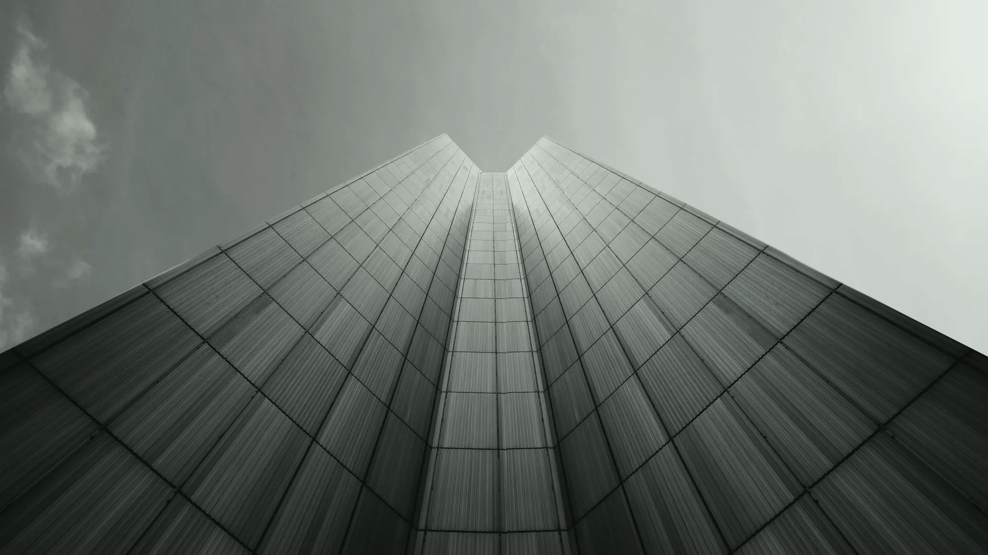 Two glass skyscrapers converging upward into a pale sky